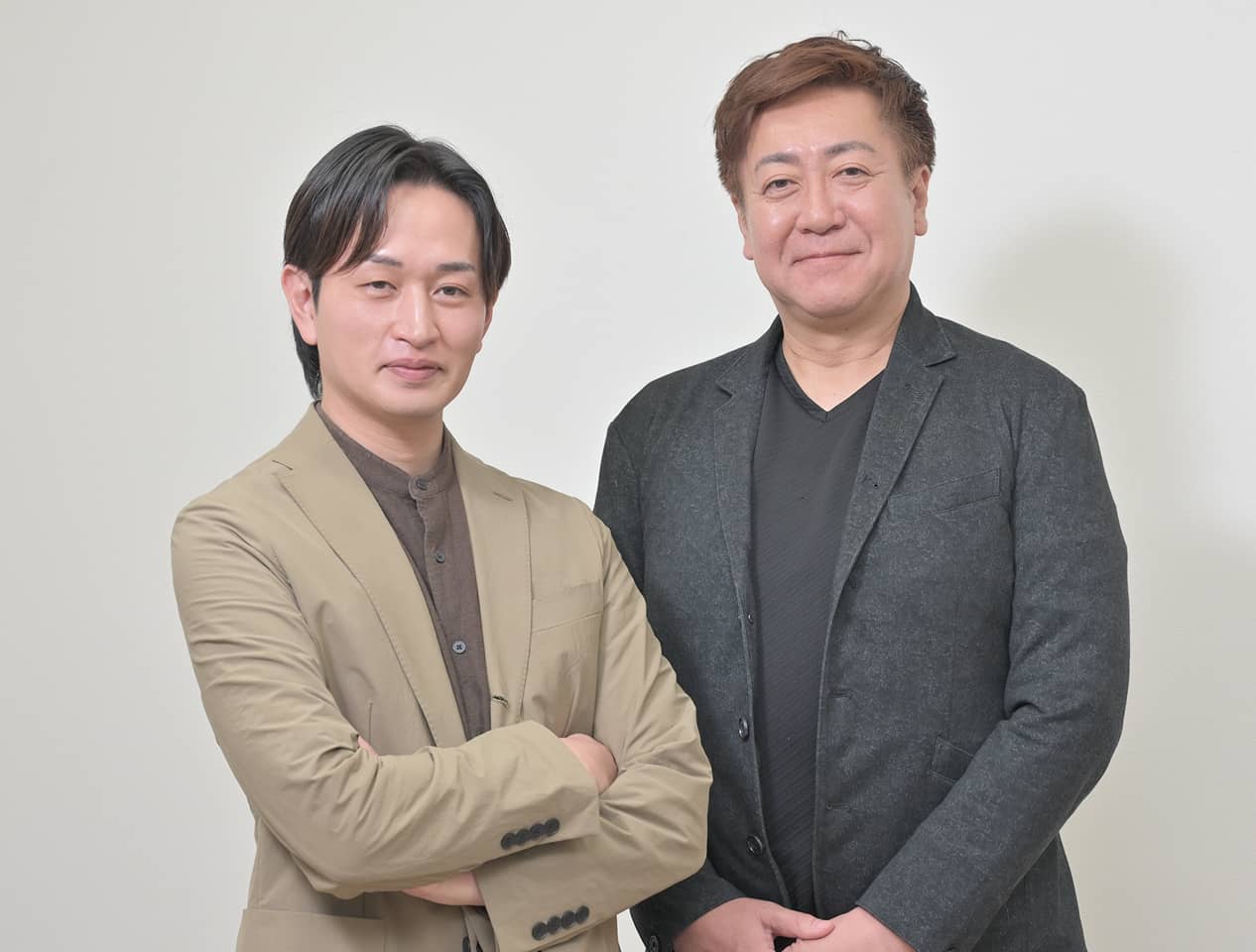 明るいベージュのジャケットとダークグレーのジャケットを着用した男性二人のポートレート写真。ビジネス向けの誠実な雰囲気で、白い背景。